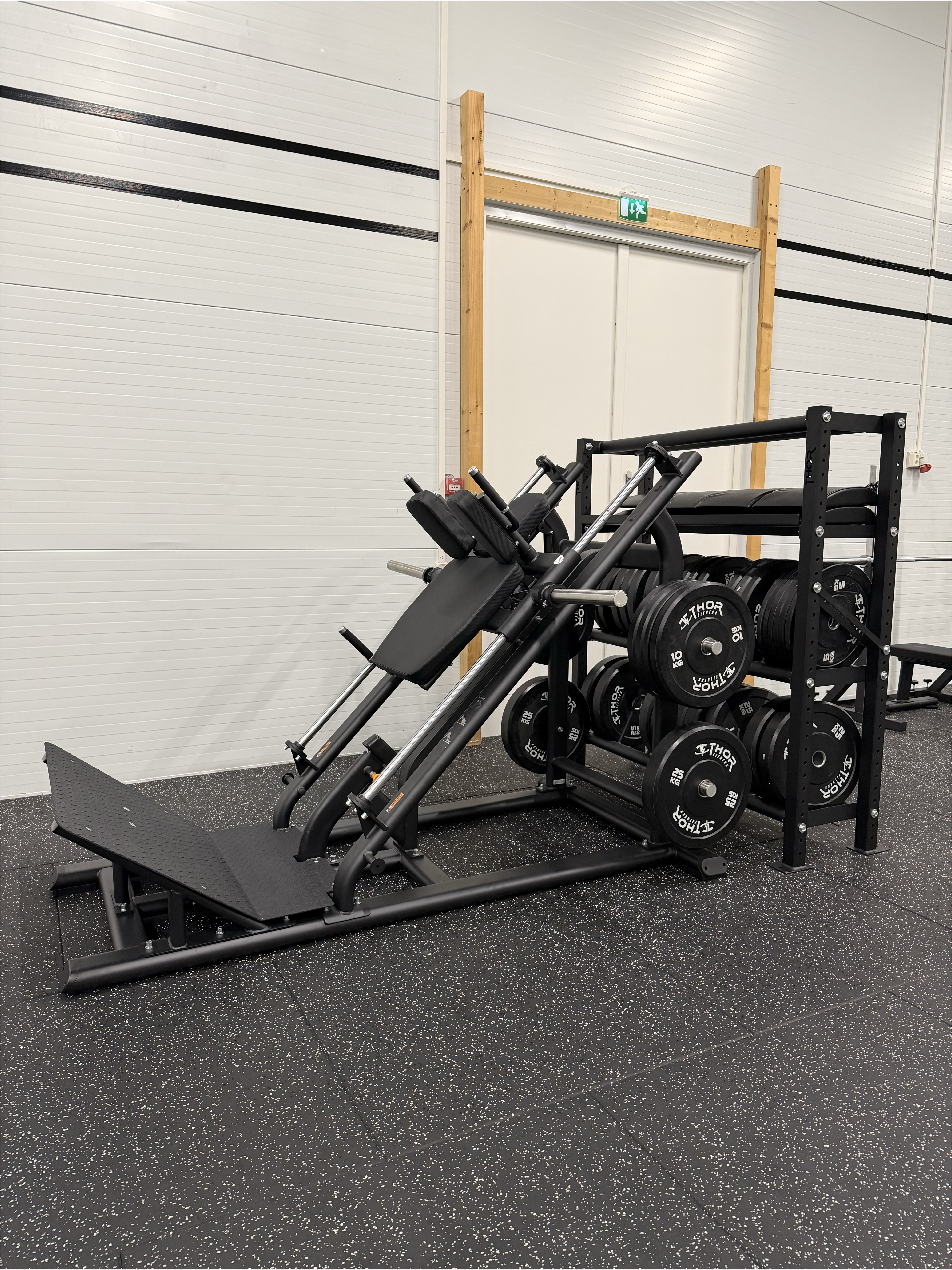 En benpressmaskin med flera viktplattor redo för användning, placerad mot en ljus vägg i gymmet.