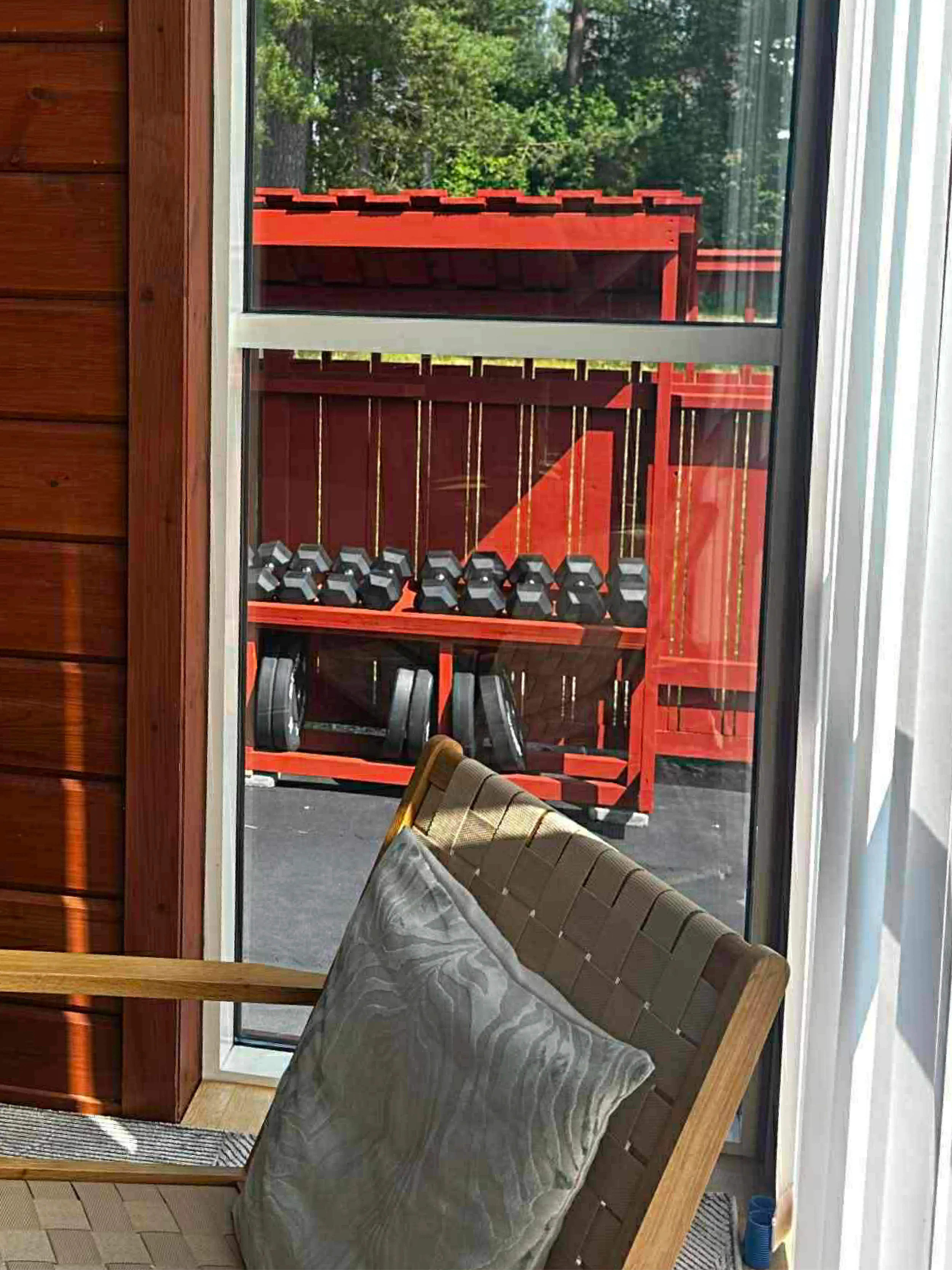 Utsikt från vilohörna inomhus mot Hälsofabrikens utegym, där hantlar och viktskivor förvaras i ett rött ställ.
