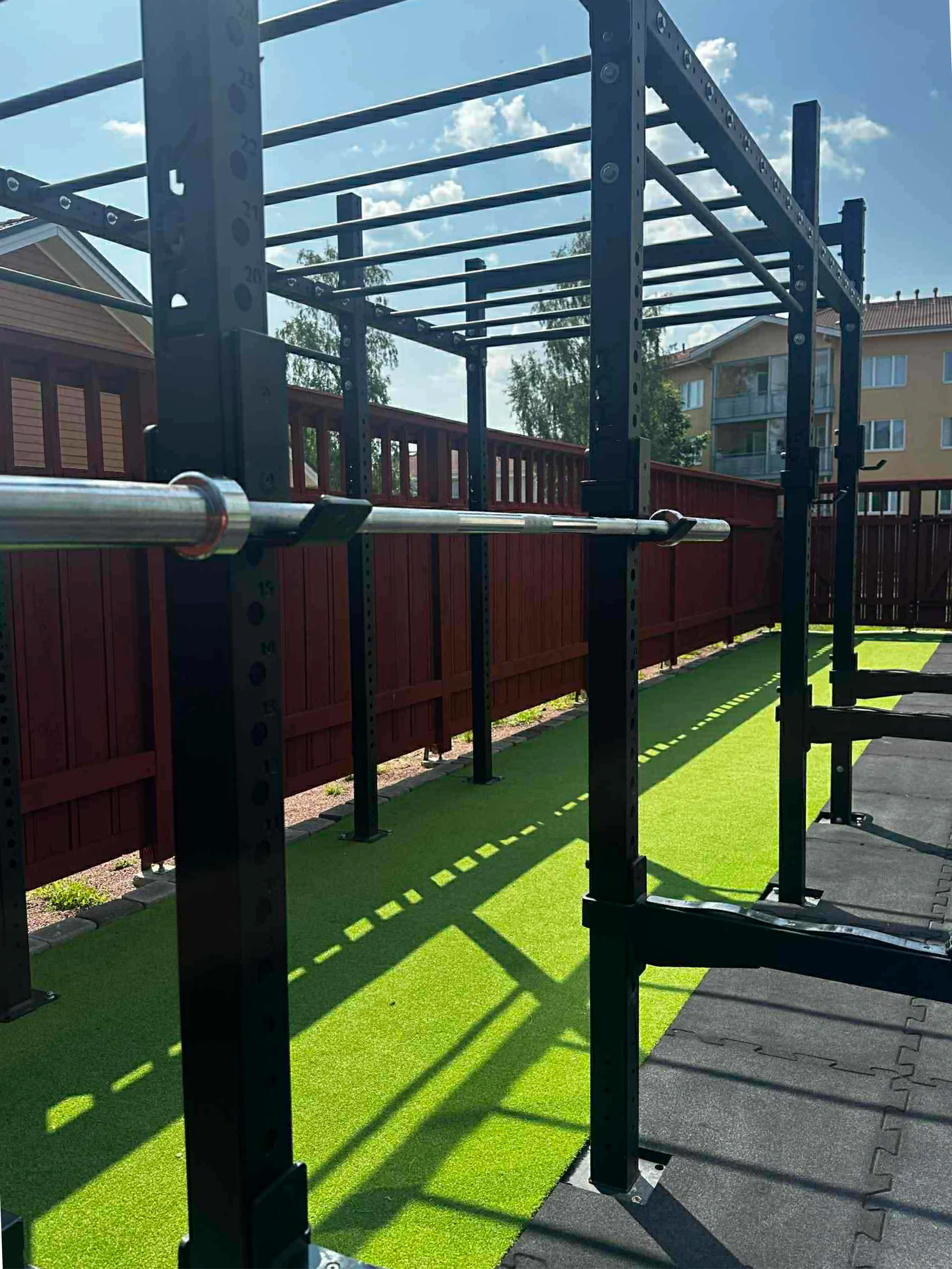 Utegymmets rigg med monkey bars, skivstång och lyftstationer mot grön konstgräs och blå himmel.